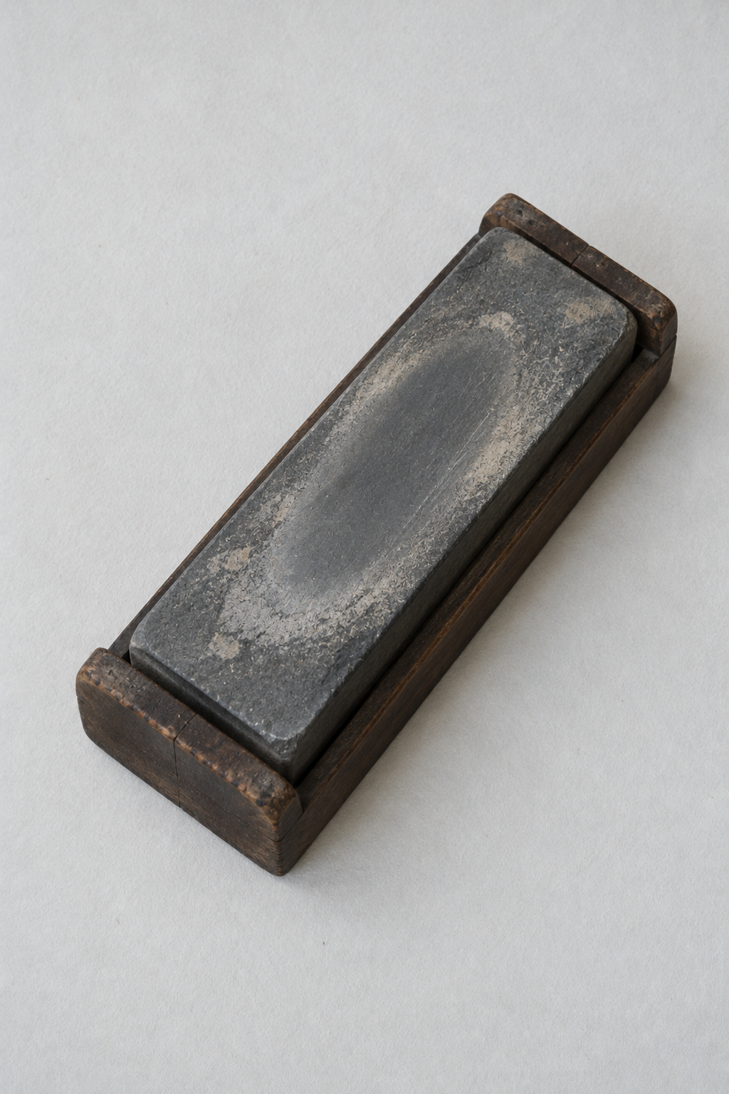 Original Just Brilliant craft study: a worn sharpening stone in a wooden cradle.