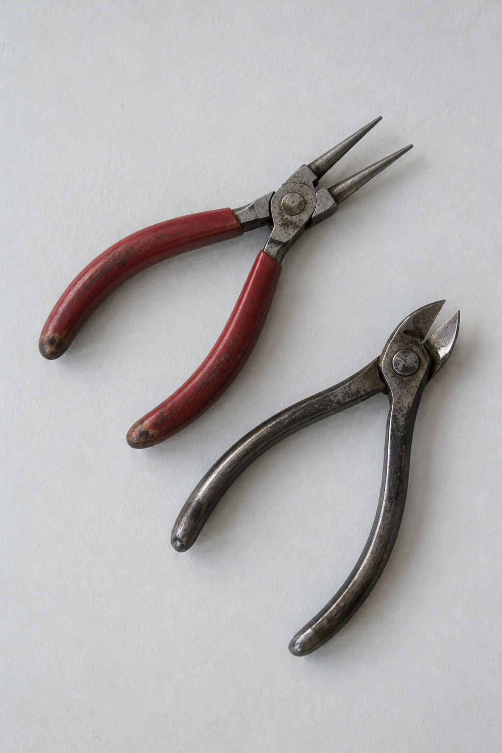 Original Just Brilliant craft study: two pairs of jeweler's pliers with worn red and steel handles.