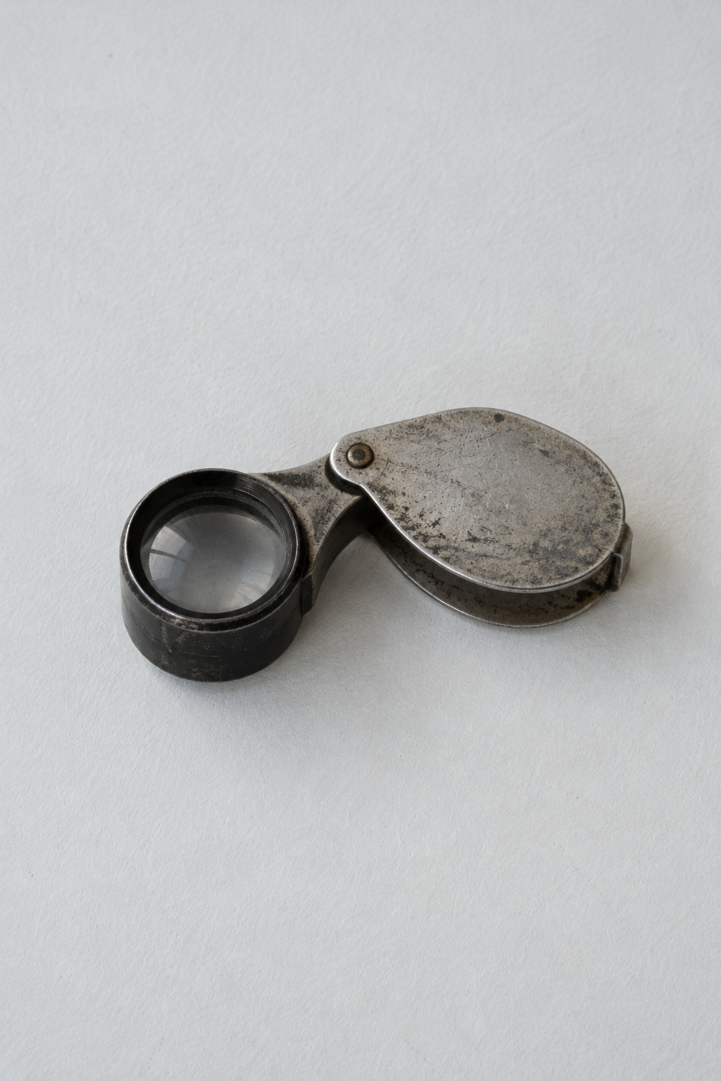 Original Just Brilliant craft study: an open folding jeweler's loupe with a worn oval cover.