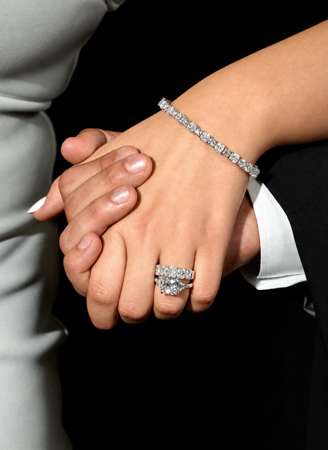 Clasped hands wearing a diamond engagement ring, wedding band and tennis bracelet.