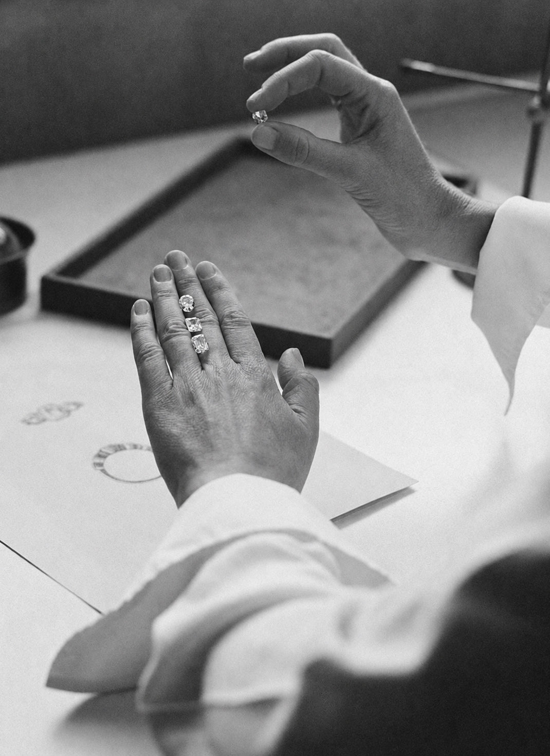 A diamond consultation with three loose stones resting in a row on the hand, photographed in black and white.